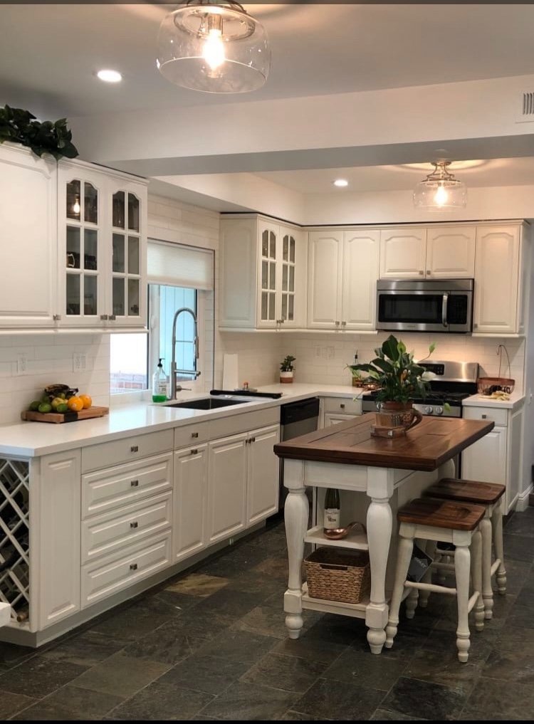 Bright white kitchen with marble countertops, glass-front cabinets, wood island with stools