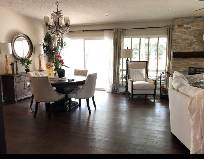 Wide view of living and dining area with chandelier, hardwood floors and stone fireplace