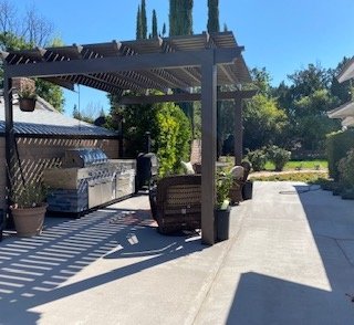 Outdoor kitchen area with dark wood pergola and built-in stainless grill