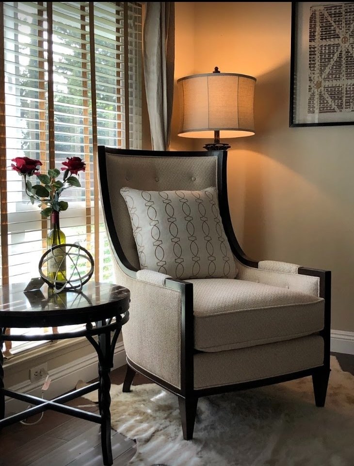 Elegant wingback reading chair with warm lamp and red roses beside large windows